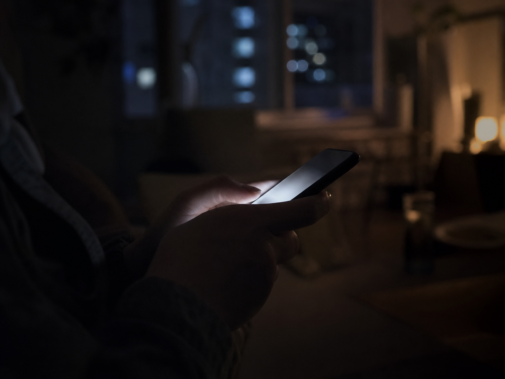 夜間にスマートフォンを手に持ち、SNSや情報サイトの投稿を閲覧している人物の手元のクローズアップ